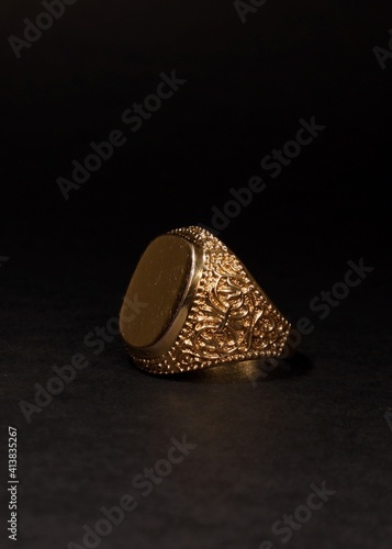 Mens gold signet ring on a black background.