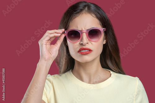 Frowning young serious woman adjusting sunglasses