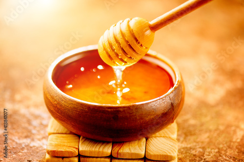 Honey dripping from honey dipper in wooden bowl.  Close-up. Healthy organic Thick honey dipping from the wooden honey spoon, closeup.