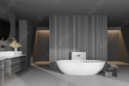 Interior of modern bathroom with gray walls  concrete floor  white bathtub and double sink with round mirror on dark gray counter.