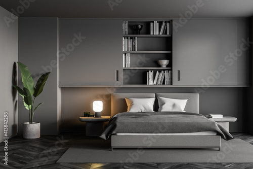 Grey bedroom with bed and linens, bookshelf and plant on parquet floor