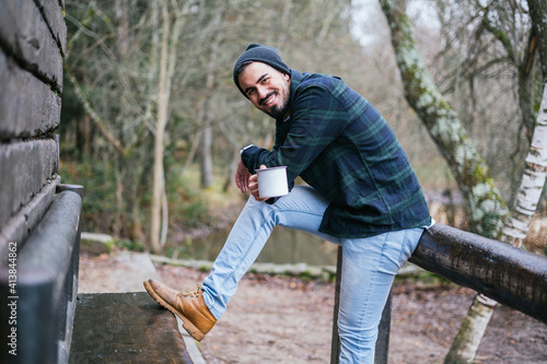 Cheerful young hipster spending leisure time drinking coffee outdoors, autumn in the countr photo