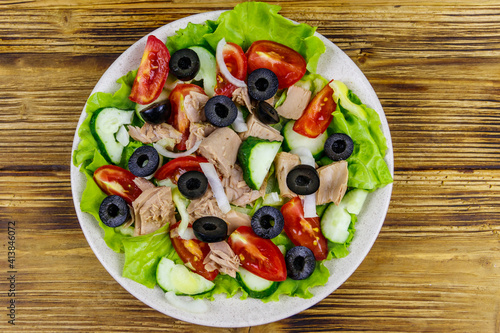 Tasty tuna salad with lettuce, black olives and fresh vegetables on wooden table. Top view