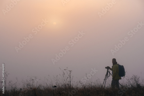 Landscape photographer taking photo in morning foggy field. Early morning foggy landscape with man silhouette photo