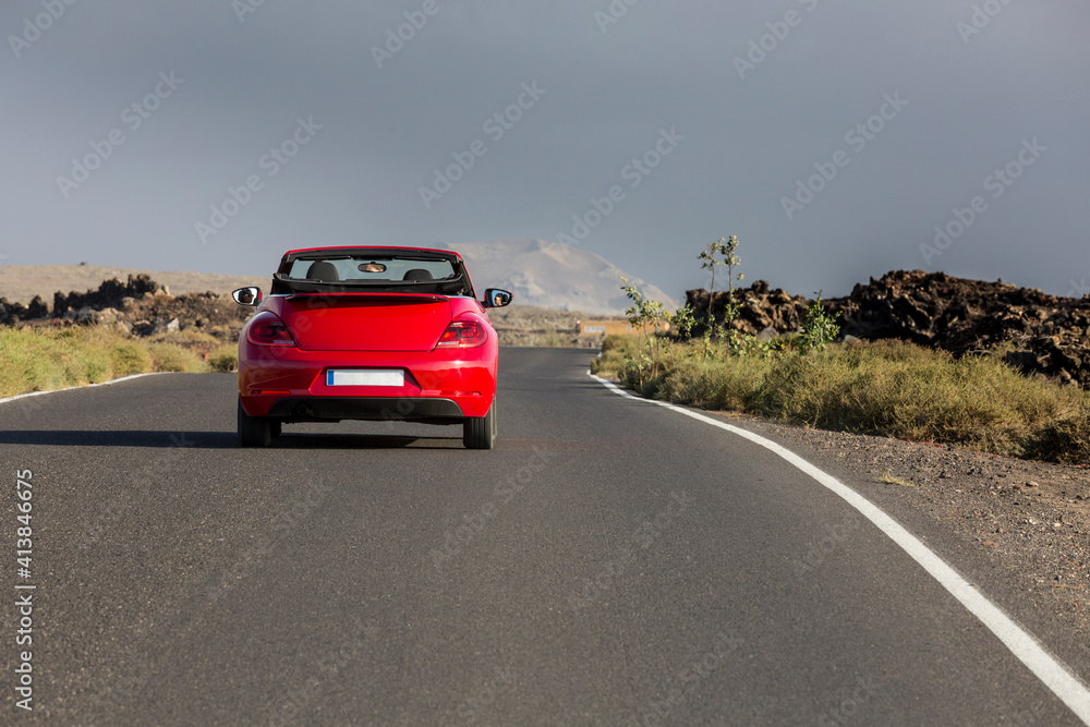 Red cabrio car driving empty paved road in desert volcanic landscape Red cabrio car driving empty paved road in desert volcanic landscape