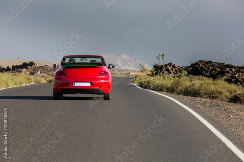 Red cabrio car driving empty paved road in desert volcanic landscape photo