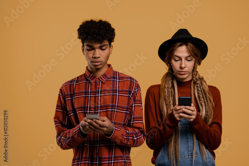 Photo of cute couple farmers watch their smartphones. Man wears plaid shirt, Woman wears denim overall and hat isolated brown color background