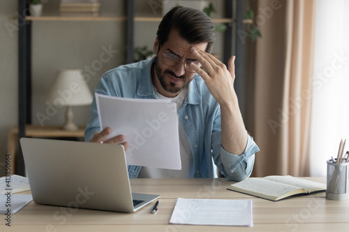 Billede på lærred Confused shocked self employed businessman holding paper letter informing about accumulated bank debt unexpected financial problem