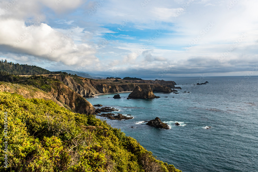 View of rocky headlands and ocean under a cloudy blue sky View of rocky headlands and ocean under a cloudy blue sky