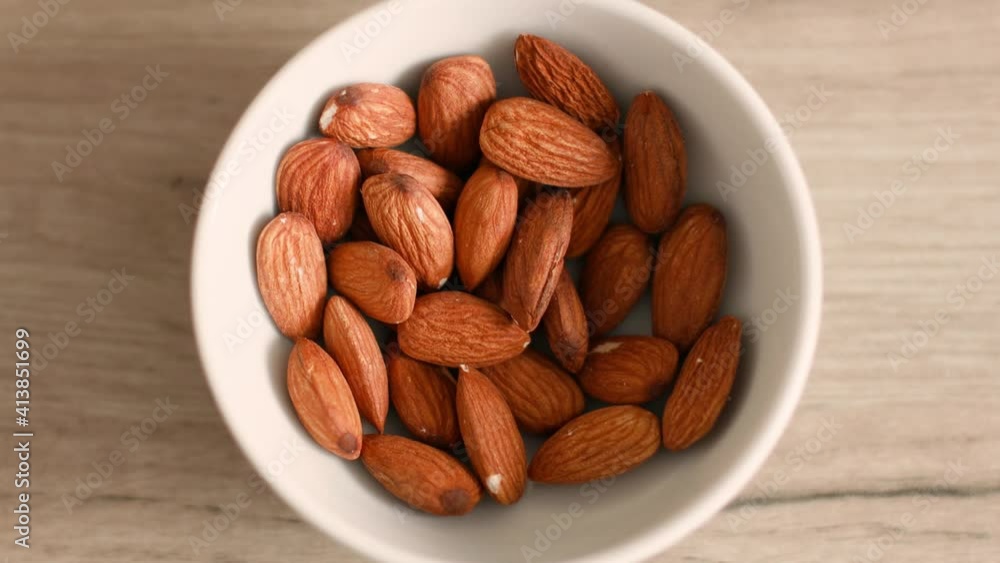 Top view of woman hand taking almonds nuts from white bowl in kitchen Top view of woman hand taking almonds nuts from white bowl in kitchen