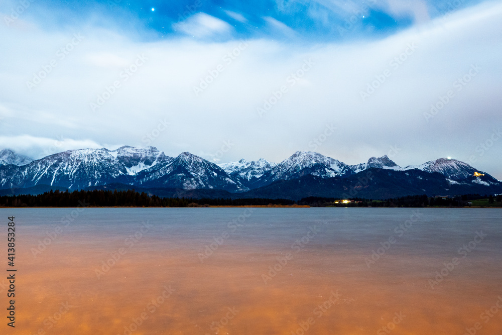 Long exposure panorama of the alps at night with the hopfensee in the foreground