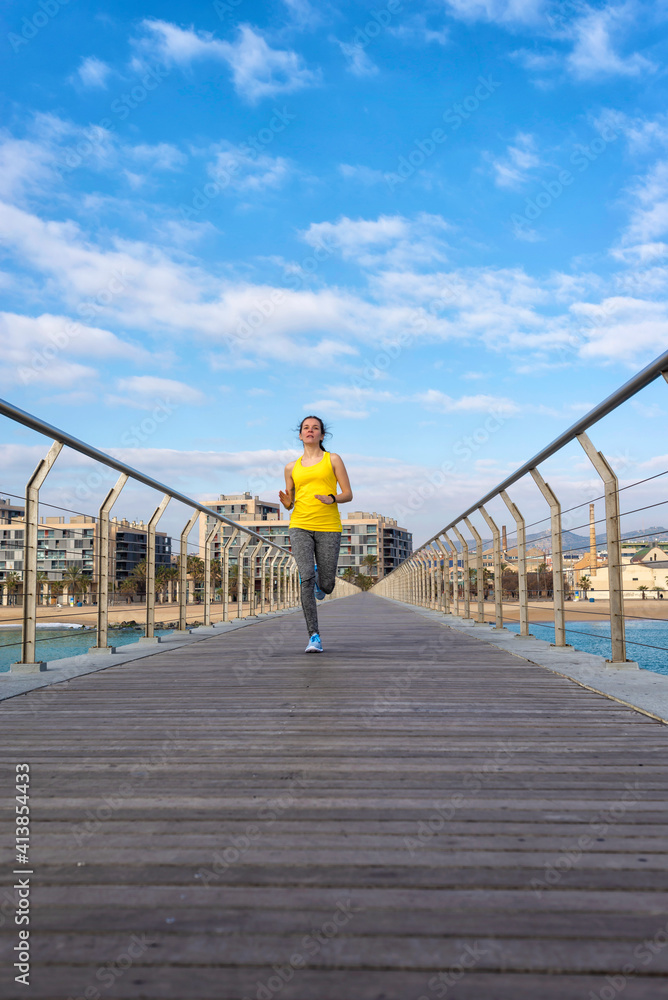 Front view of fit sportive woman running on pier against blue sky Front view of fit sportive woman running on pier against blue sky