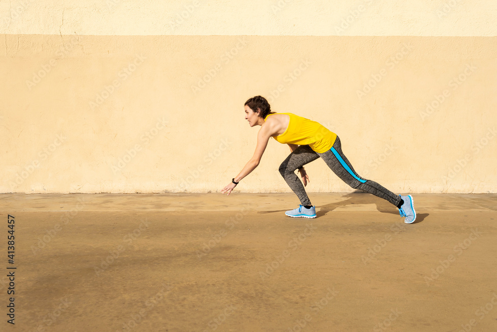 Athletic woman in sportswear running on paved street against wall Athletic woman in sportswear running on paved street against wall