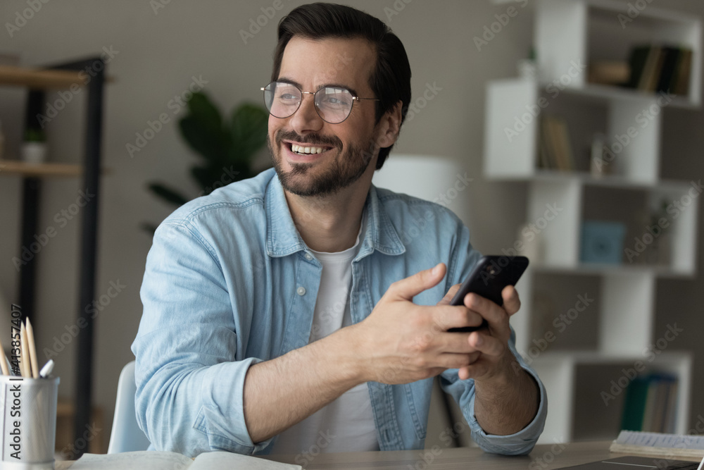 Dreamer. Inspired young man sit at table holding cell look at distance excited with new opportunity offered by business email. Happy motivated millennial male enjoy good news received at phone message Dreamer. Inspired young man sit at table holding cell look at distance excited with new opportunity offered by business email. Happy motivated millennial male enjoy good news received at phone message