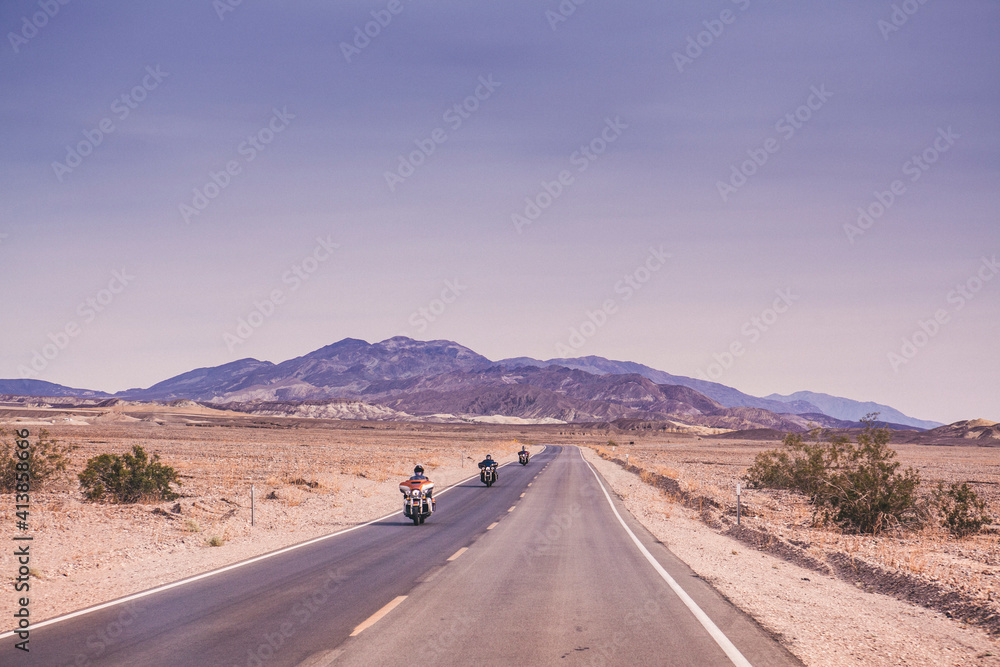 Three motorbikes ride on a straight road in Death Valley National Park Three motorbikes ride on a straight road in Death Valley National Park