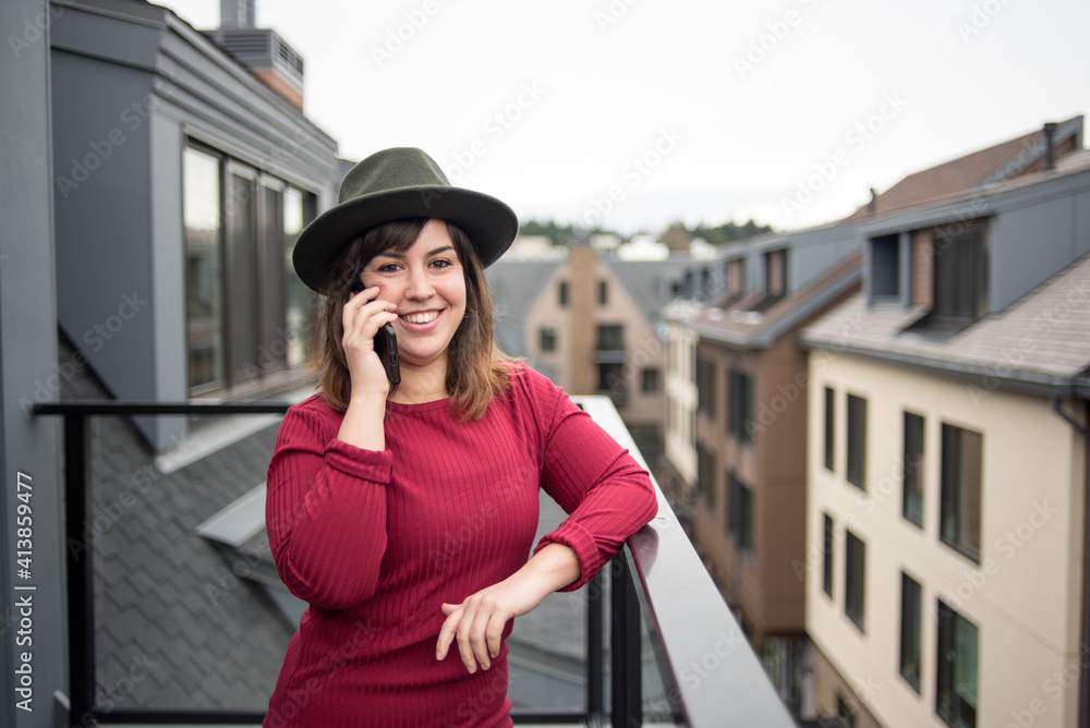 Woman on rooftop balcony talking on phone with city view behind her Woman on rooftop balcony talking on phone with city view behind her