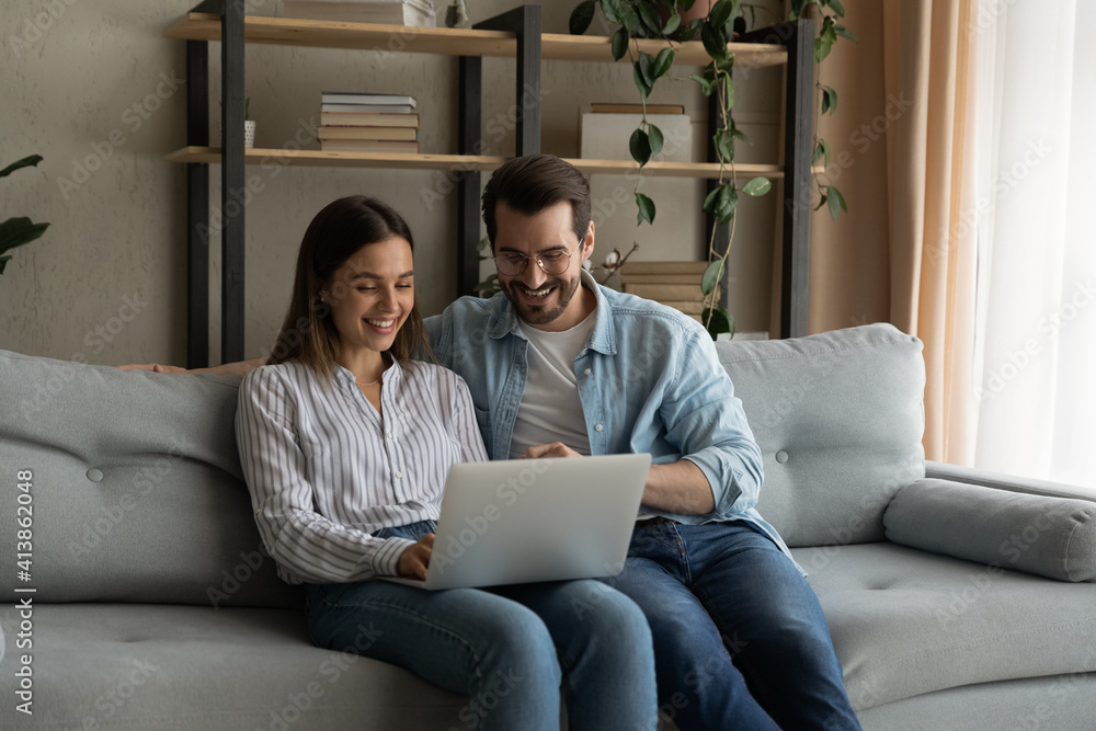 Happy husband wife newlyweds rest on sofa hold laptop choose furniture for new home buy consumer goods online. Young family couple using pc discuss flat renovation options planning trip on vacation Happy husband wife newlyweds rest on sofa hold laptop choose furniture for new home buy consumer goods online. Young family couple using pc discuss flat renovation options planning trip on vacation