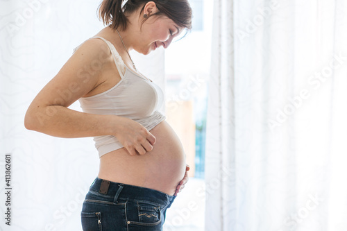 Free Download Happy pregnant mother in blue jeans is hugging her naked tummy, close up - GFXLoad