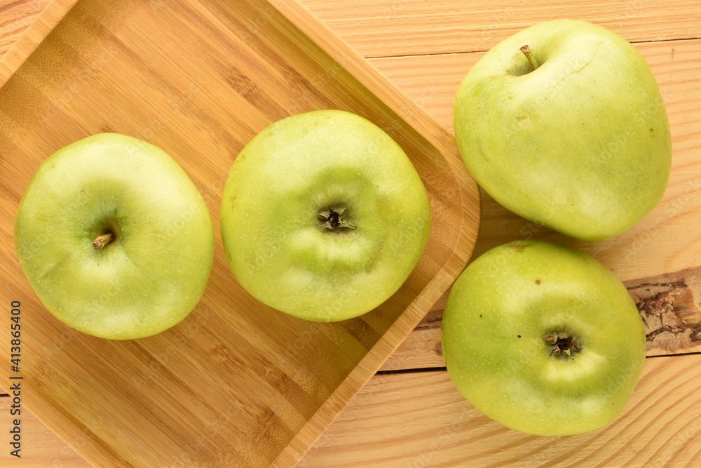 Several ripe green apples in a bamboo dish on a wooden table, close-up, top view. Several ripe green apples in a bamboo dish on a wooden table, close-up, top view.