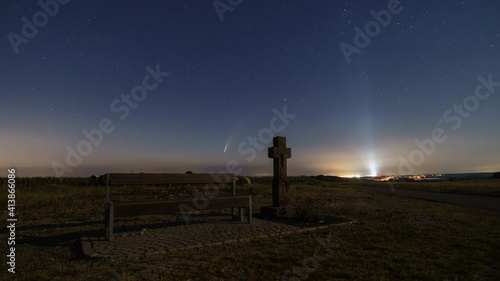 The Neowise comet in the night sky with resting bench and stone way cross with air base Spangdahlem in background, Germany photo