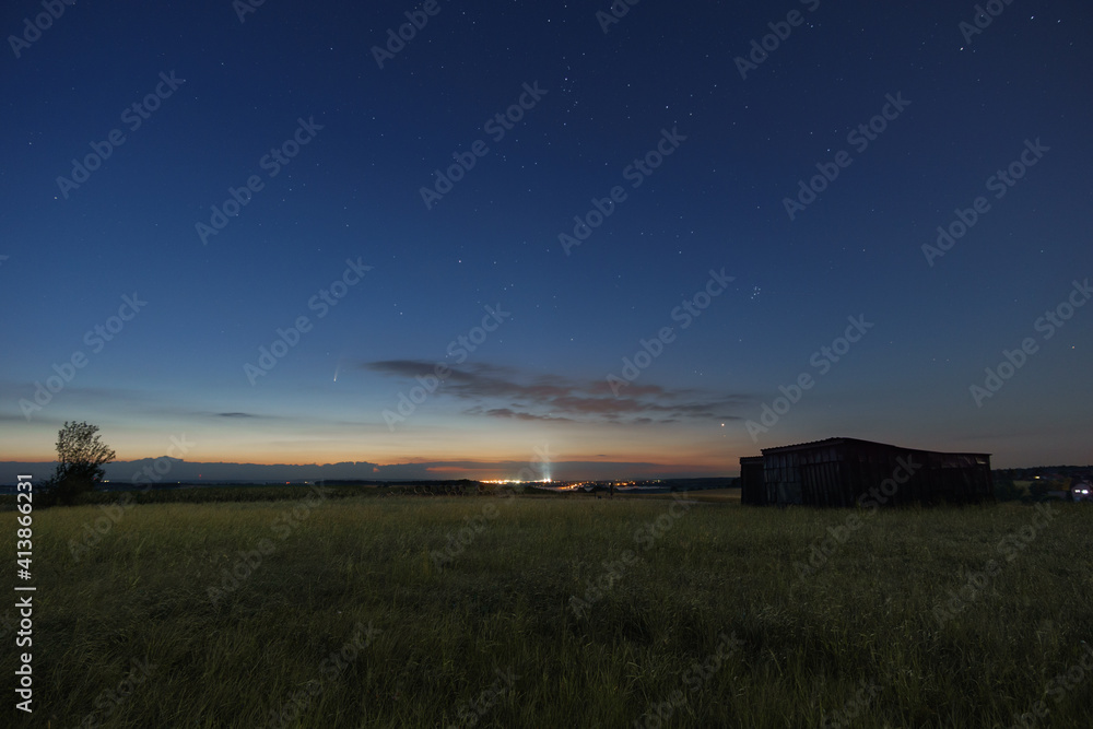 Fototapeta premium The Neowise comet in the night sky over meadow with wooden barn in morning twilight before sunrise in the Eifel, Germany