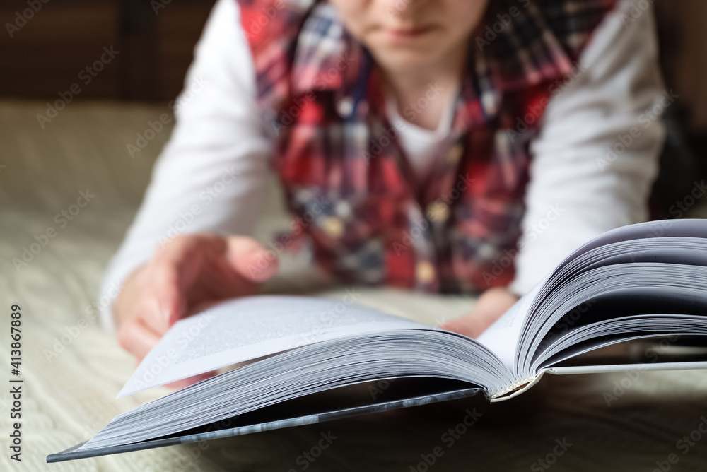 Woman dressed in casual home clothes lays on bed reading book. Selective focus on book Woman dressed in casual home clothes lays on bed reading book. Selective focus on book