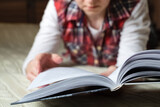 Woman dressed in casual home clothes lays on bed reading book. Selective focus on book