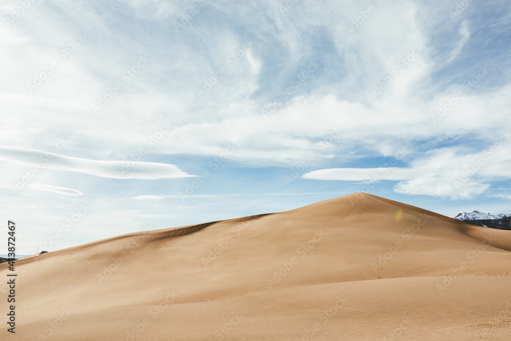 golden sand dune rises into blue sky with wispy clouds golden sand dune rises into blue sky with wispy clouds