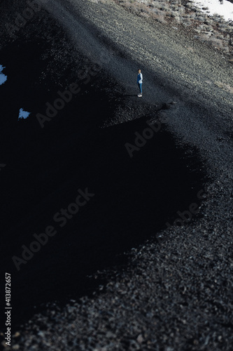 woman stands on the edge of a volcanic black sand basin photo