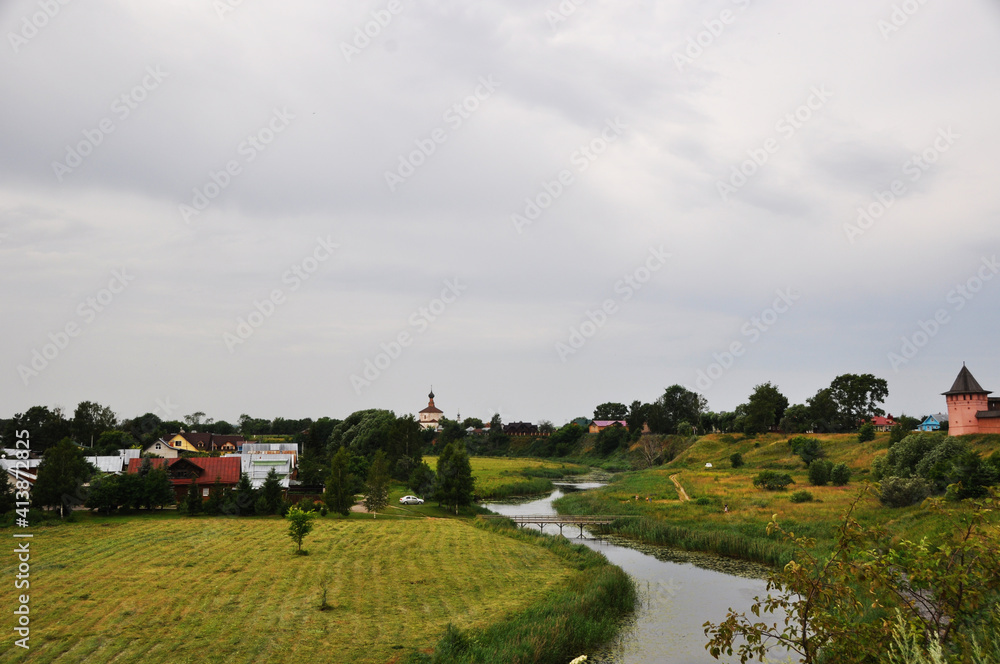 Obraz premium Panoramic views of log houses, river and green fields.