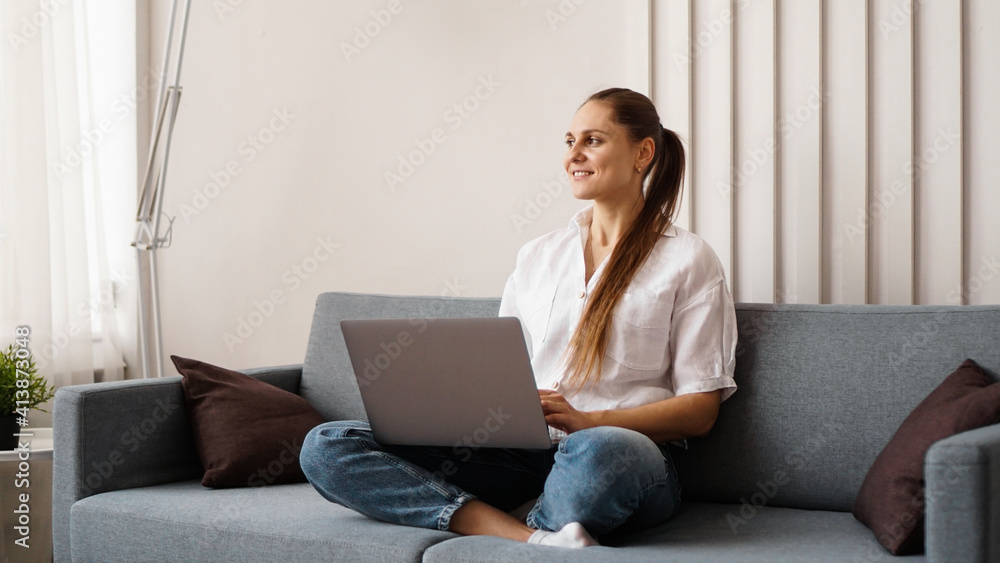 Fototapeta premium Woman working on laptop from home or student studying from home or freelancer. Modern business woman in a white shirt and jeans.