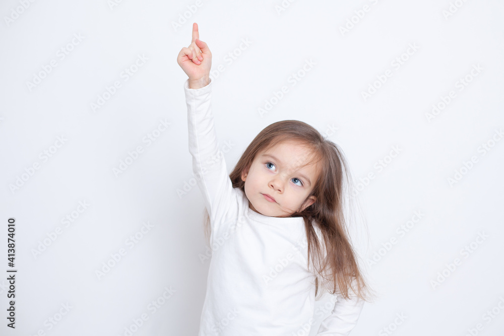 Fototapeta premium Portrait of a girl on a white background with her hand and finger raised up. Blue eyes. Russ hair. Bright tones. Points up
