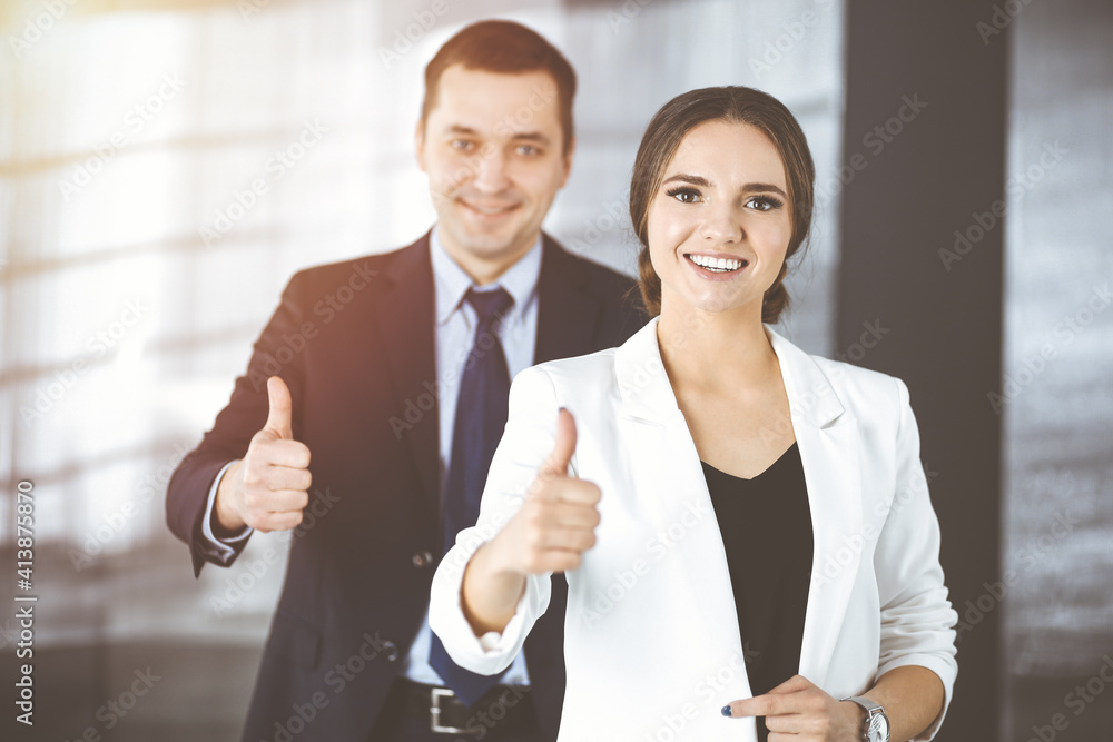 Smiling businesspeople are happy with a good result of their teamwork, standing with thumbs up in a sunny modern office. Concept of business success Smiling businesspeople are happy with a good result of their teamwork, standing with thumbs up in a sunny modern office. Concept of business success