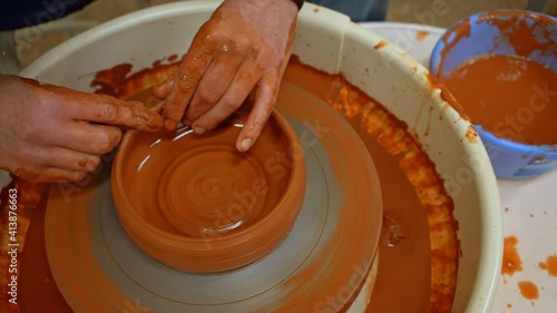 Potter sculpts a clay bowl on a potters wheel (Close-up). Close-up of hands of a potter shaping a clay bowl