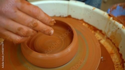 An artisan potter sculpts a clay bowl using a wooden scraper and sponge. The video shows the process of creating ceramic products using special pottery tools