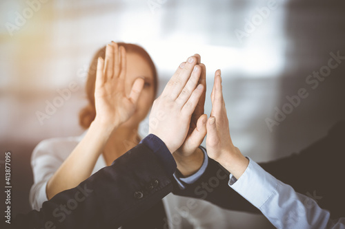 Young businesspeople are celebrating success of their project, standing in a sunny modern office. Unknown businessmen are giving five to each other. Business success concept