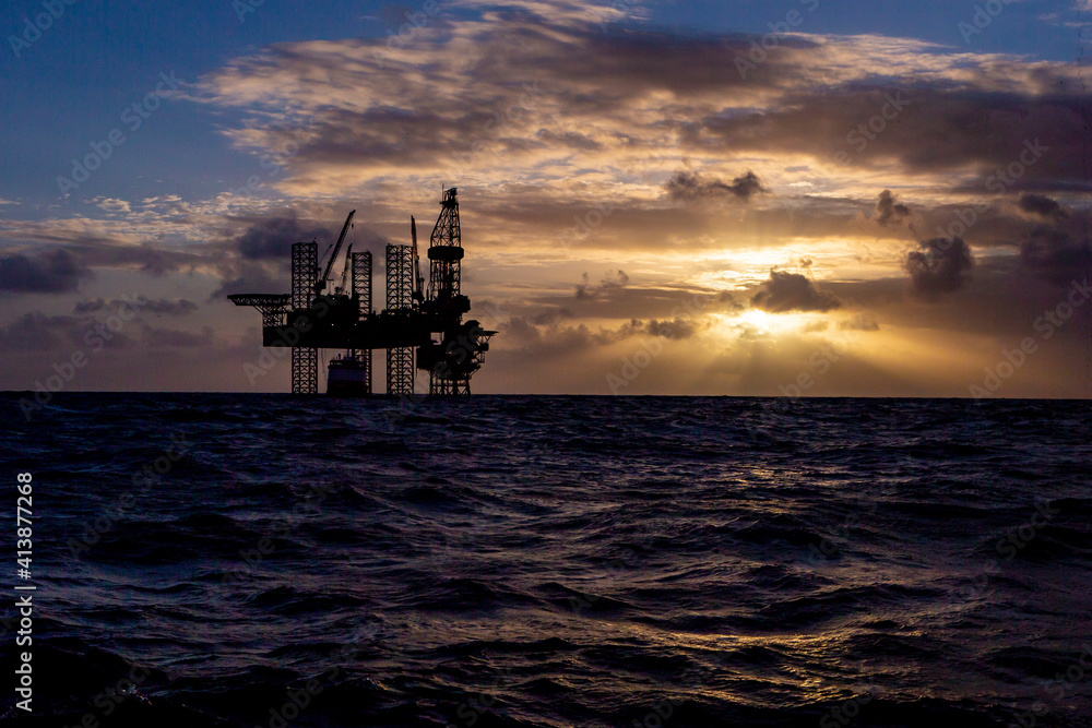 Offshore drilling platform during sunrise with work vessel Offshore drilling platform during sunrise with work vessel