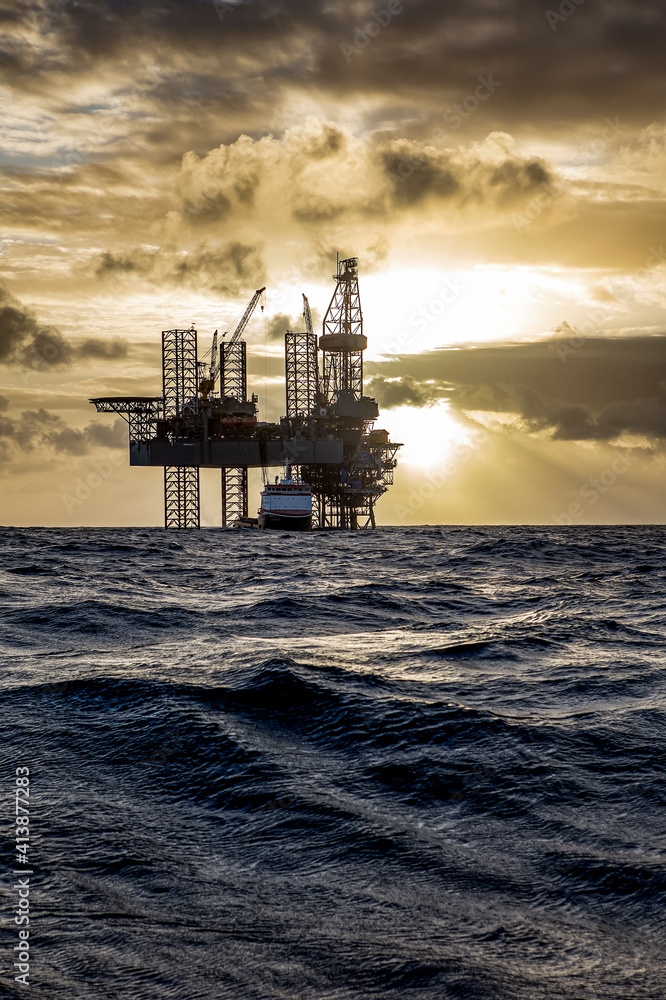 Offshore drilling platform during sunrise with work vessel Offshore drilling platform during sunrise with work vessel