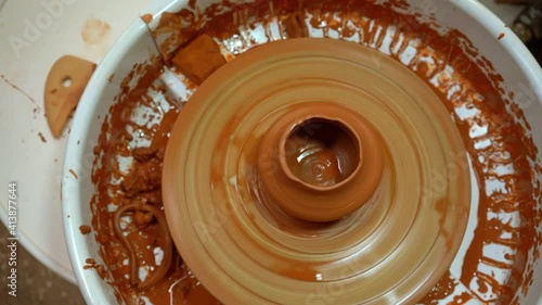 A potter's wheel with an orange clay jug is rotating (top view). The clay product rotates on a pottery wheel in the workshop