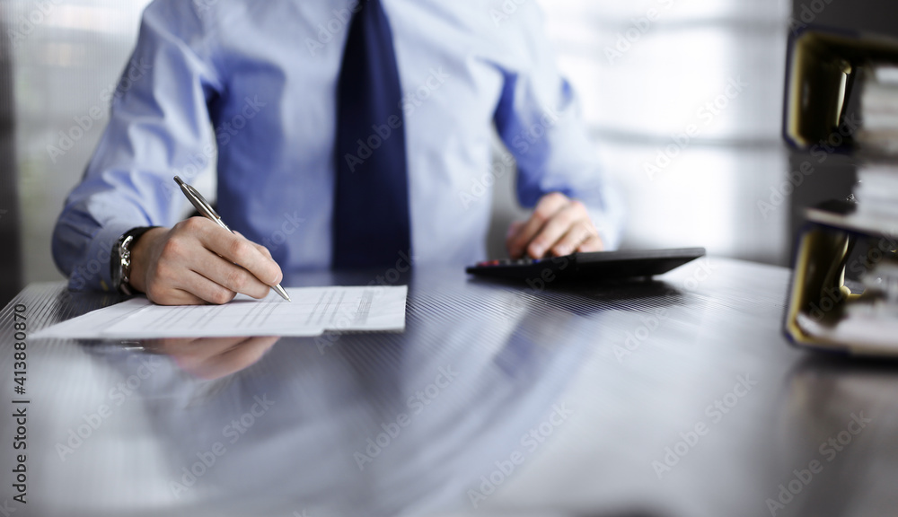 Unknown man accountant in blue shirt use calculator and computer with holding pen on while staying at home during covid pandemic. Taxes and audit concept Unknown man accountant in blue shirt use calculator and computer with holding pen on while staying at home during covid pandemic. Taxes and audit concept