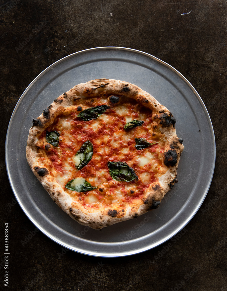 Artisan pizza on grey metallic plate against brown background Artisan pizza on grey metallic plate against brown background