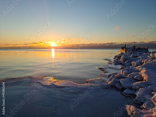 Fototapeta Naklejka Na Ścianę i Meble -  Winter Baltic sea and ice covered frozen breakwaters at dawn. Baltic sea - sandy winter beach with frozen breakwaters, white foam, waves on sunset. Scenic landscape Baltic sea in polar winter