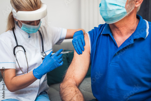 Female doctor vaccinating senior male patient at home. Coronavirus, Covid-19 concept.