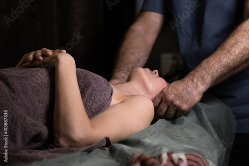 Professional facial massage. Male masseur makes procedures on a female face on a dark background.