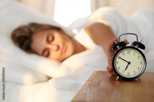 Sleepy young woman stretching hand to ringing alarm willing turn it off. Early wake up, not getting enough sleep, getting work concept