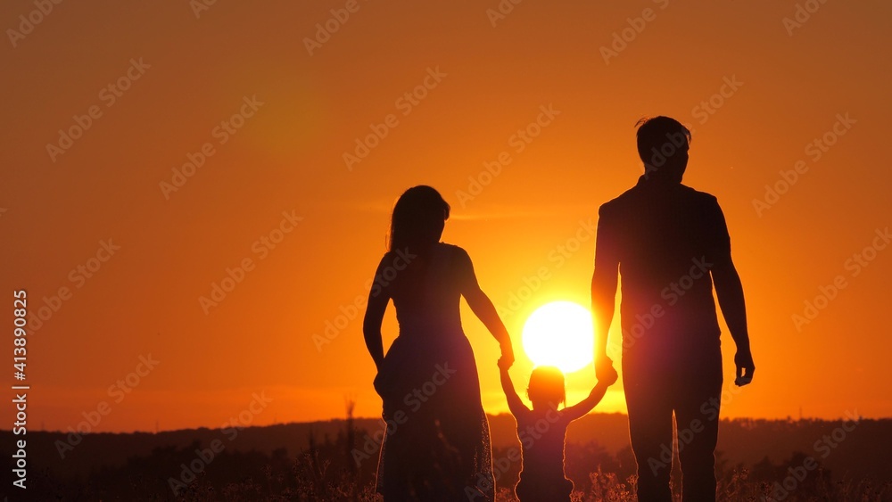 Happy family, little daughter is jumping, holding hands of dad and mom in park in sun. The child plays with dad and mom on field in light of sunset. Walk with small child in nature. childhood