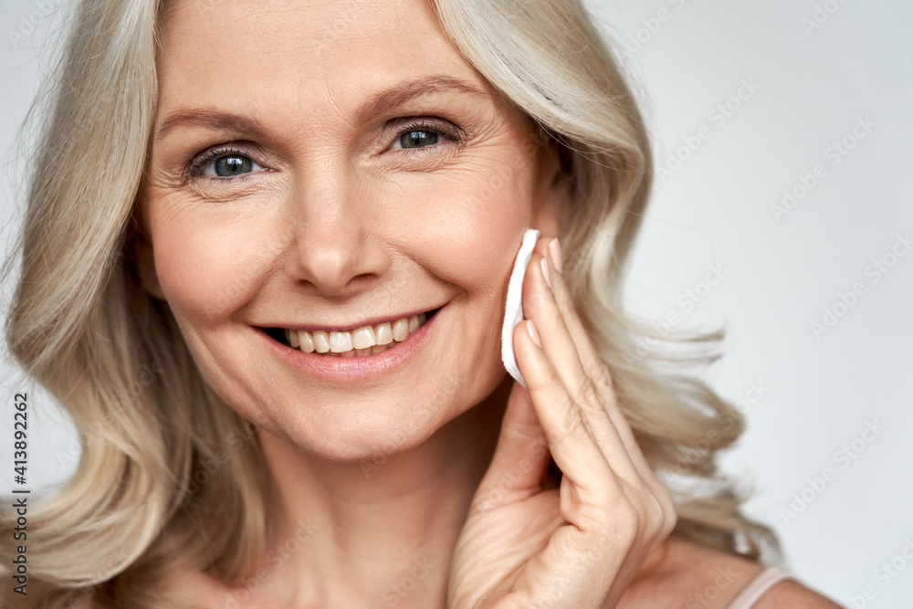Smiling 50s middle aged older woman holding cotton pad sponge cleansing face skin with cleanser, happy mature lady removing makeup enjoy healthy clean anti age dry skincare beauty treatment. Smiling 50s middle aged older woman holding cotton pad sponge cleansing face skin with cleanser, happy mature lady removing makeup enjoy healthy clean anti age dry skincare beauty treatment.