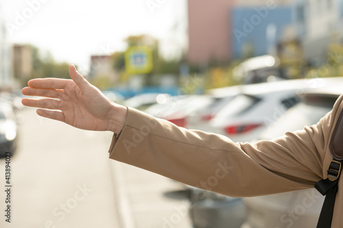 Arm of young contemporary busy female in beige trenchcoat trying to catch taxi
