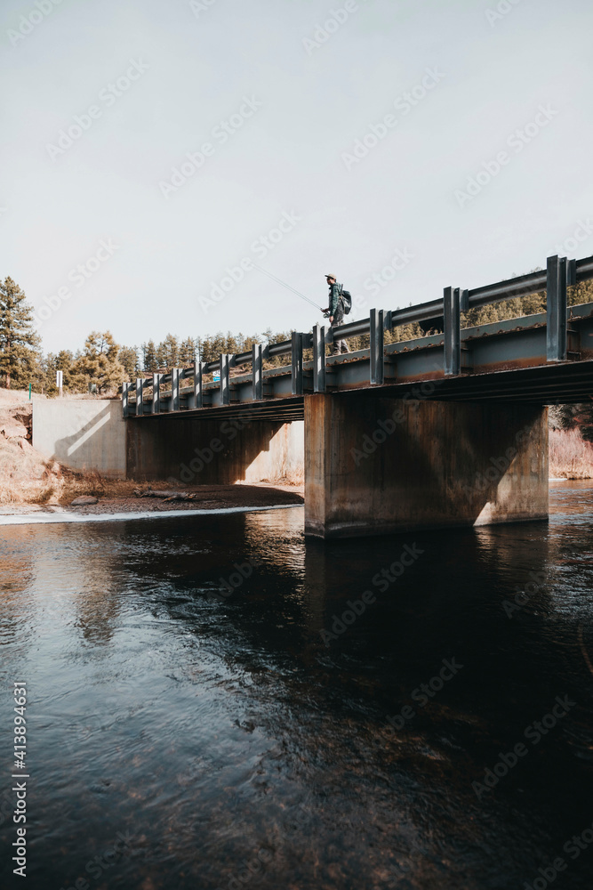 Low angle view of hiker with fishing rod standing on bridge over river against clear sky Low angle view of hiker with fishing rod standing on bridge over river against clear sky