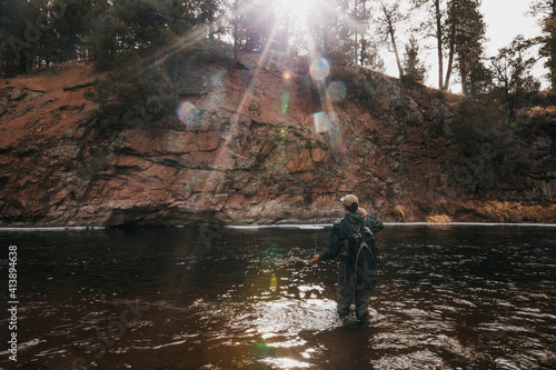 Rear view of male hiker with backpack fishing in river by mountain photo